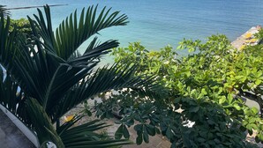 Une vue sur la côte, avec un ciel dégagé, un quai où est amarré un bateau, et une végétation luxuriante.