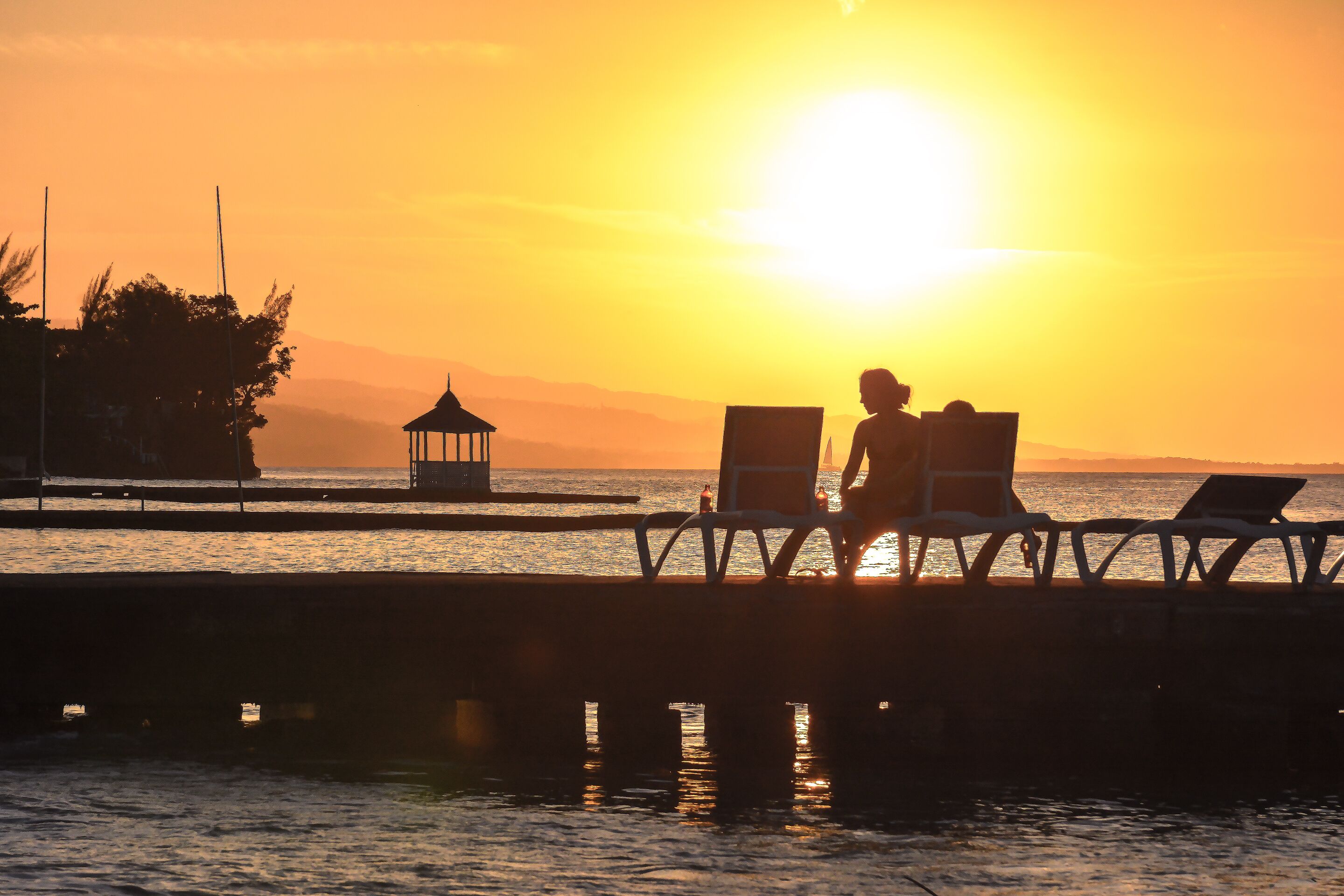 Vista al atardecer desde un muelle con dos sillones mirando al agua.