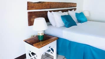 A bed with white and blue bedding, a wooden headboard, a white nightstand with a lamp, and a colorful artwork on the wall.