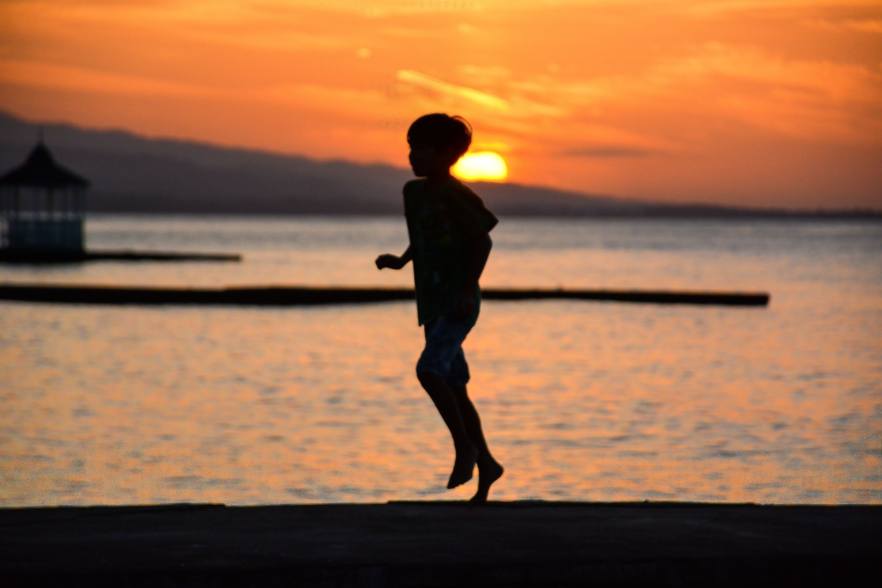 Silueta de un niño corriendo por un muelle al atardecer.