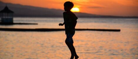 Silueta de un niño corriendo por un muelle al atardecer.