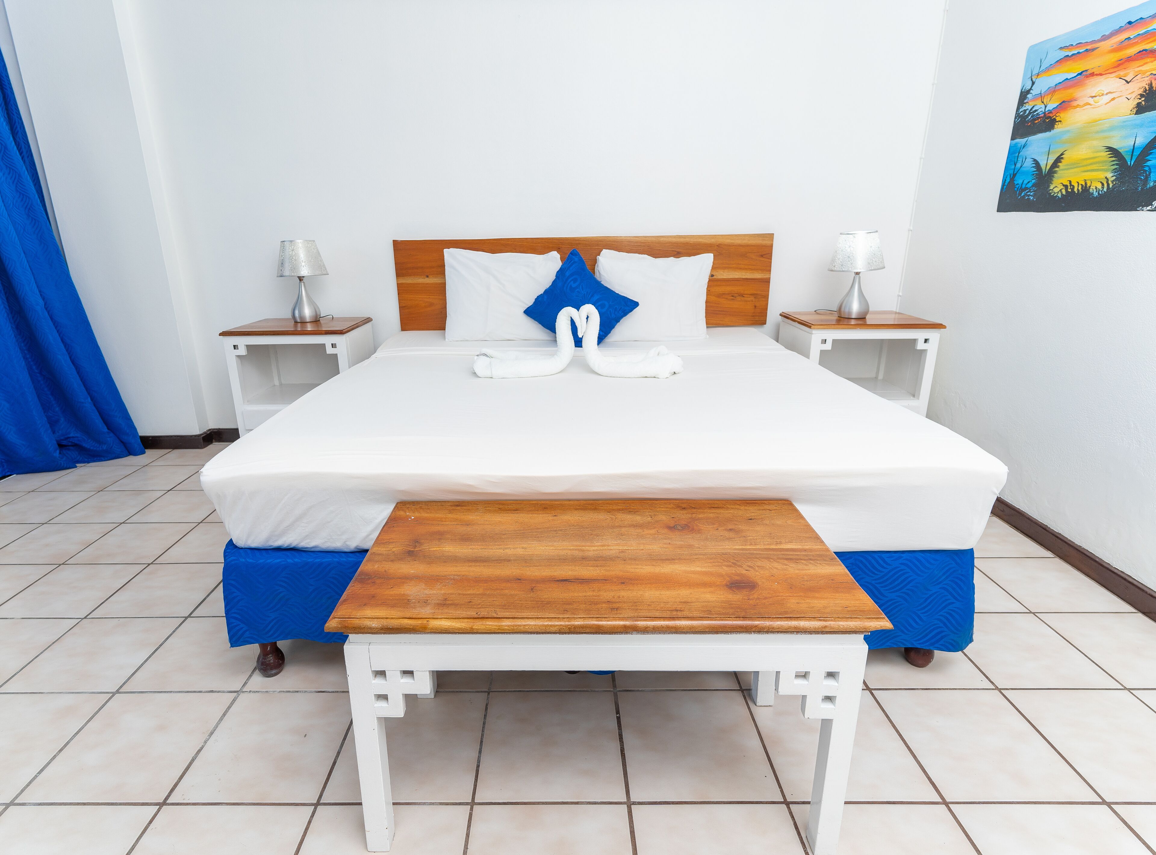 A neatly arranged hotel room with a large bed, two bedside tables, and a wooden bench at the foot of the bed.