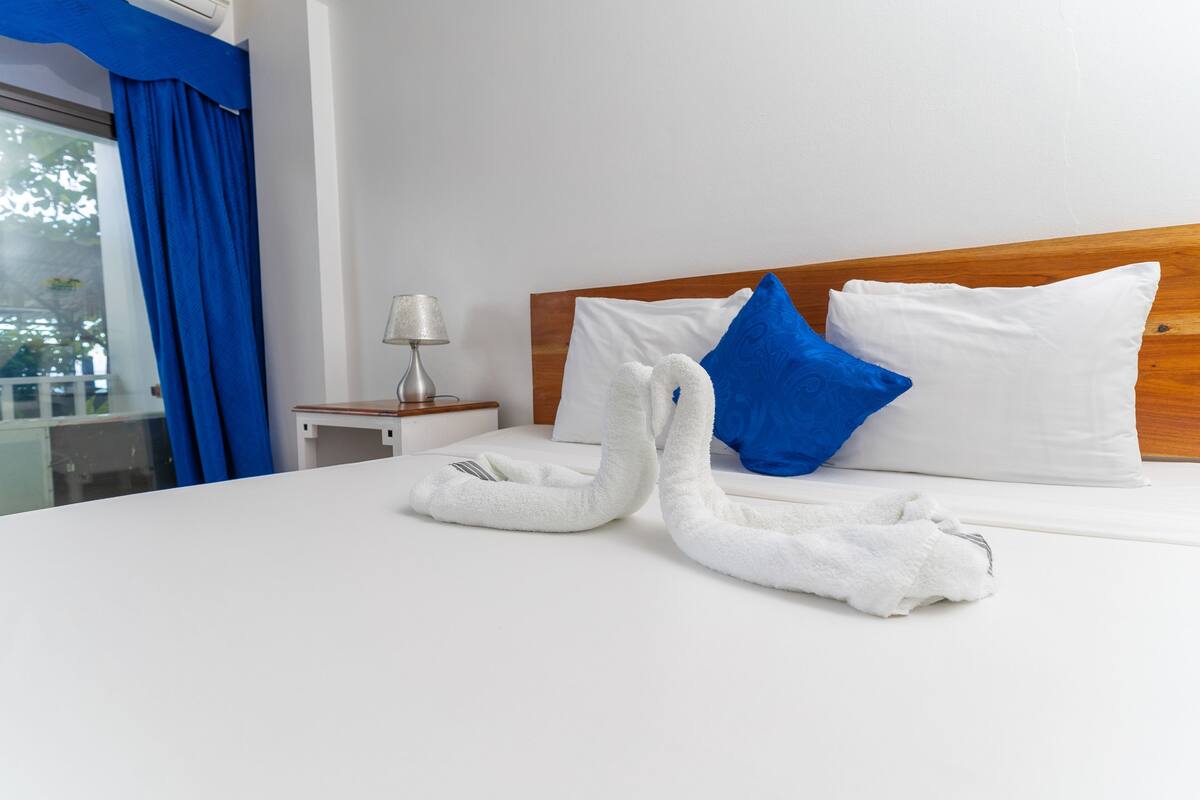 A neatly made bed with white and blue pillows, a wooden headboard, and a white towel folded on the bed.