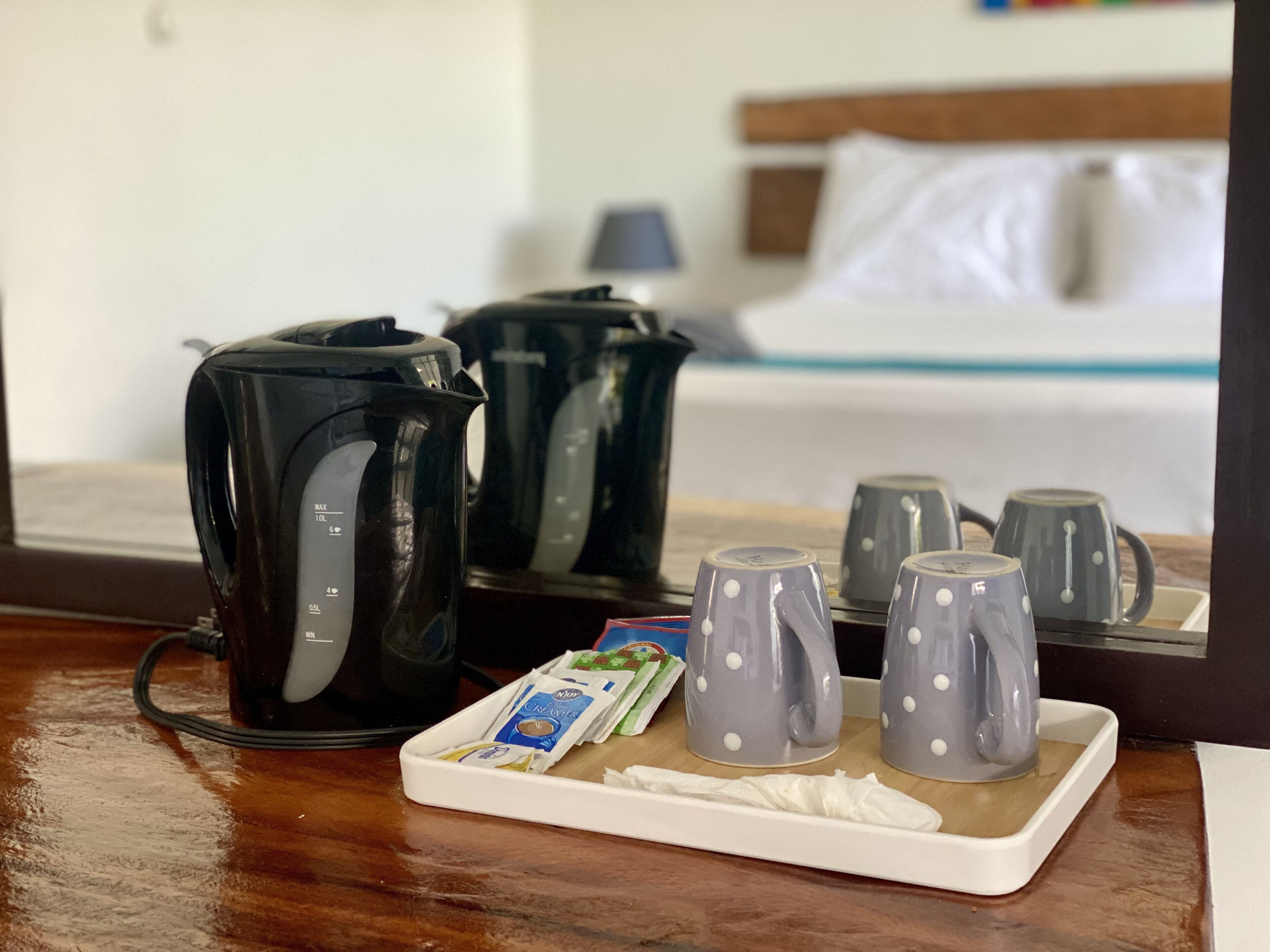 A hotel room with a wooden table, a tray with a coffee maker, cups, and a packet of creamer.