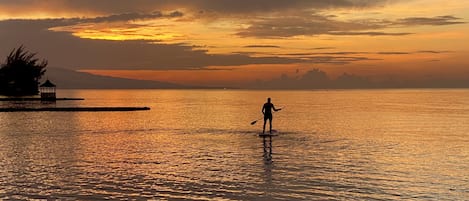 A person paddleboarding on calm water during sunset.