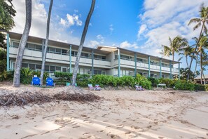 A beachfront hotel with multiple balconies, palm trees, and beach chairs.