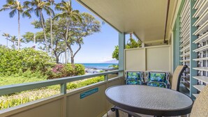 A balcony with a view of the ocean and palm trees, a round table, and a sign indicating a smoking area. - Aloha Condos, Napili Bay Resort, Condo 110, Beach View (Lahaina)