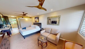 A modern hotel room with a bed, a sofa, a glass coffee table, and a ceiling fan.