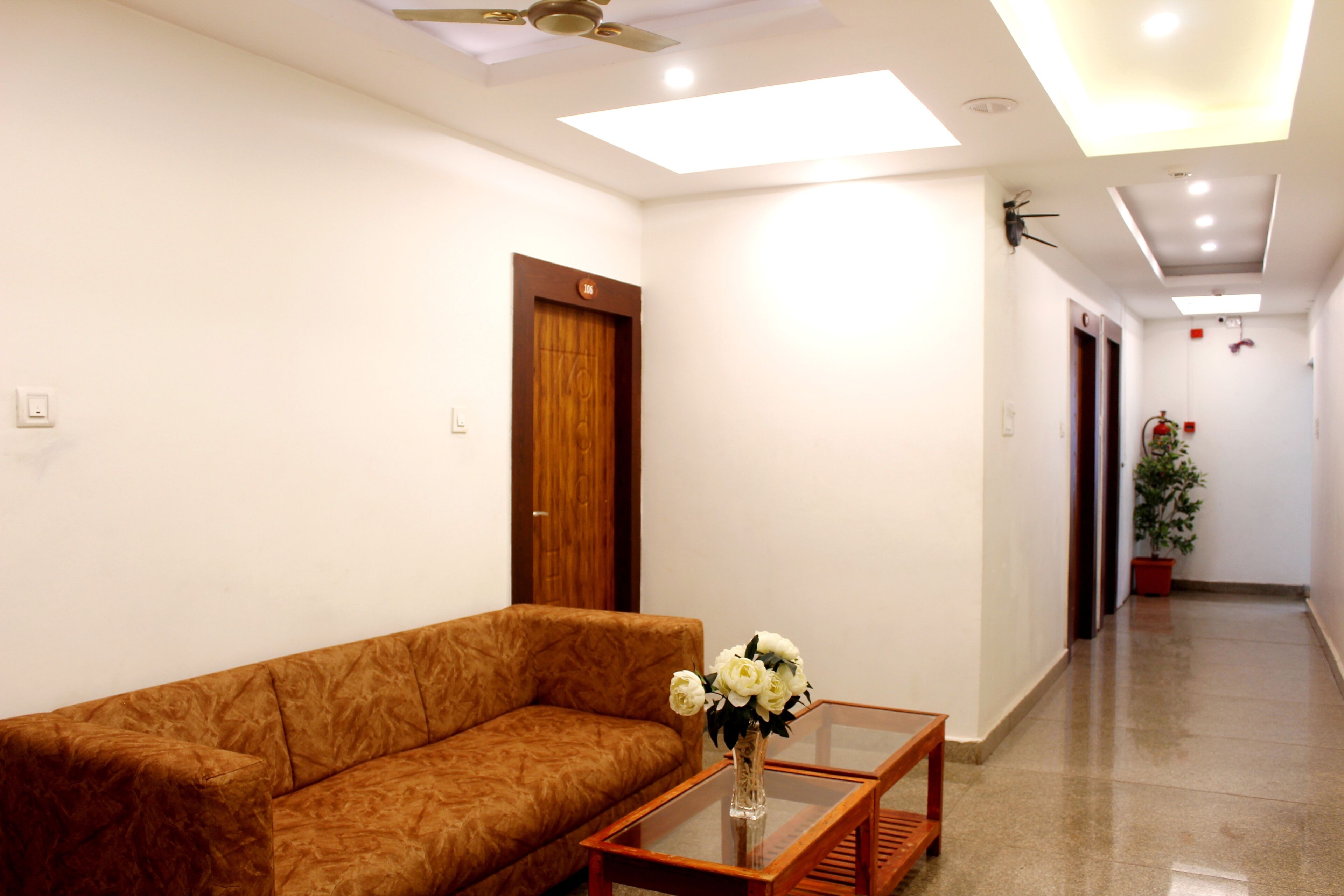 A modern hotel lobby with a brown sofa, a glass-top coffee table with a vase of flowers, and a potted plant.