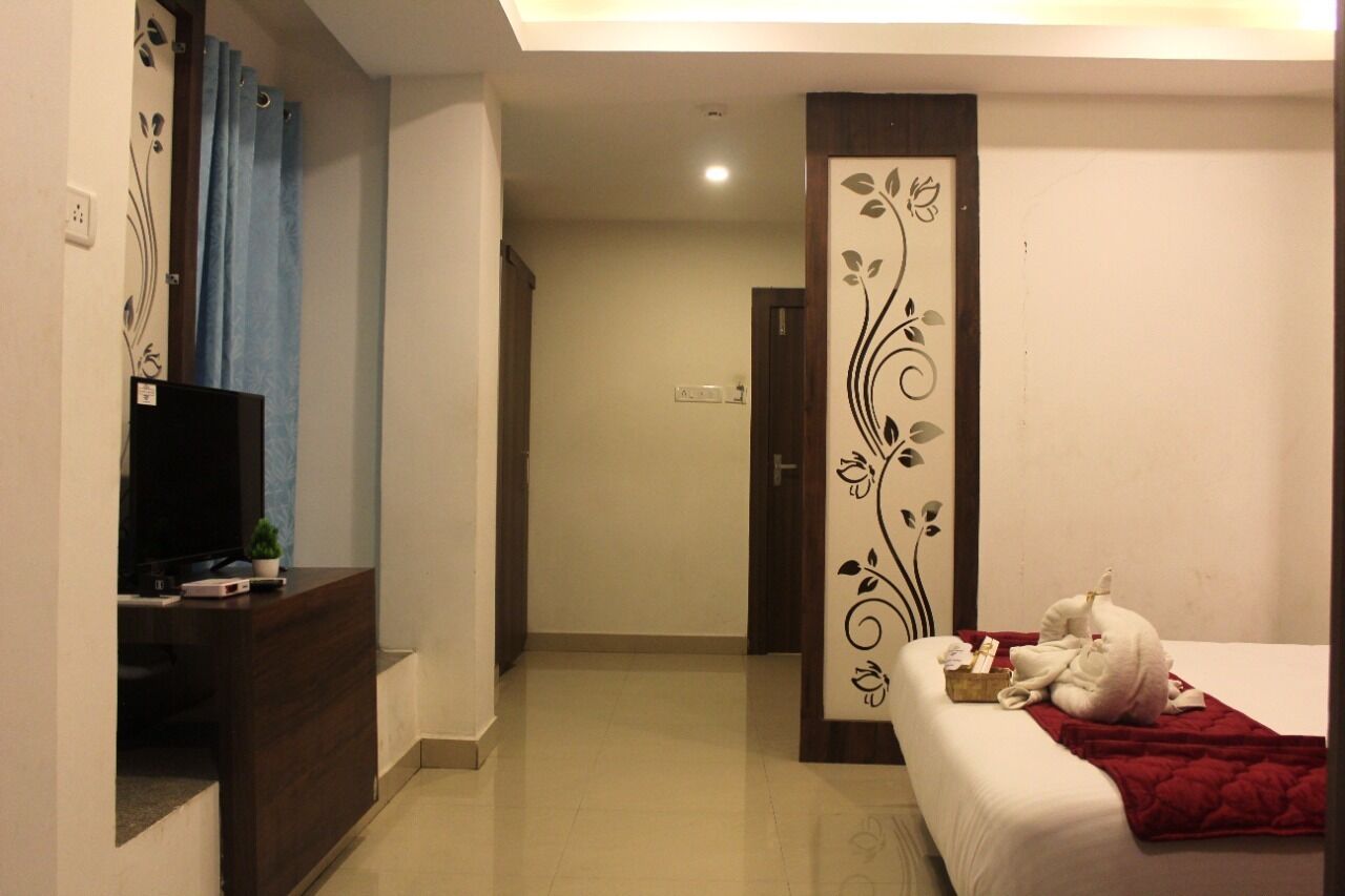 A hotel room with a bed, a TV on a desk, a decorative panel, and a red blanket on the bed.