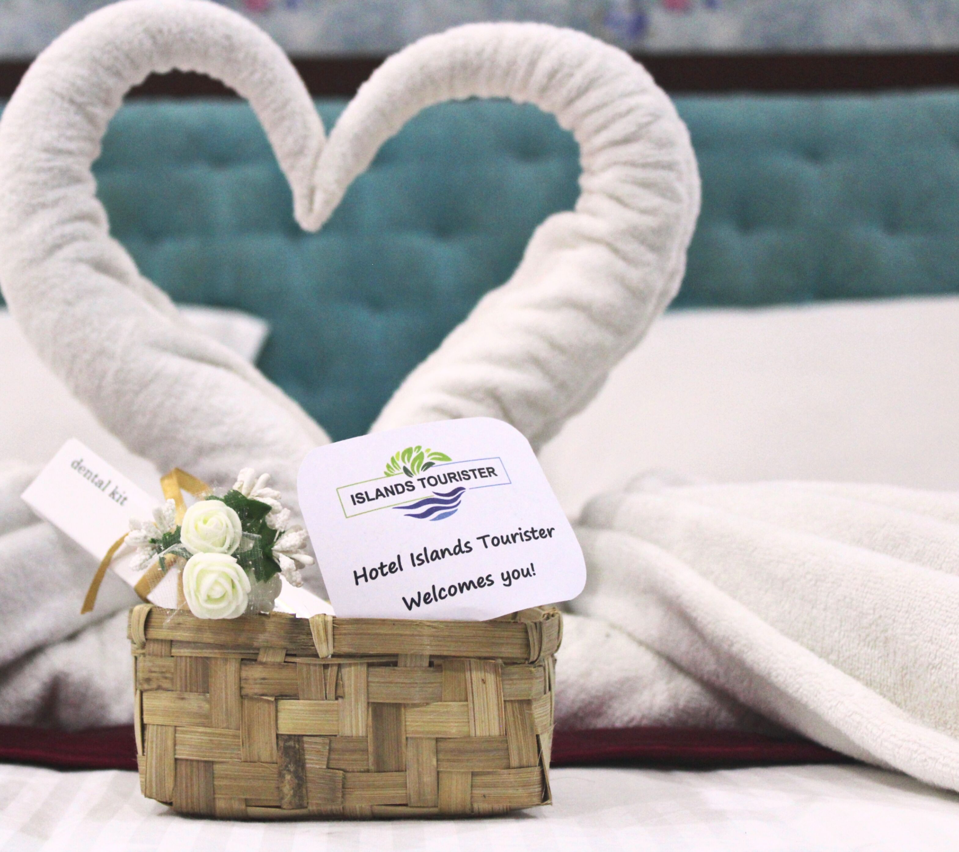 Una cesta de mimbre con una toalla con forma de corazón y un cartel de bienvenida para Hotel Islands Tourist.
