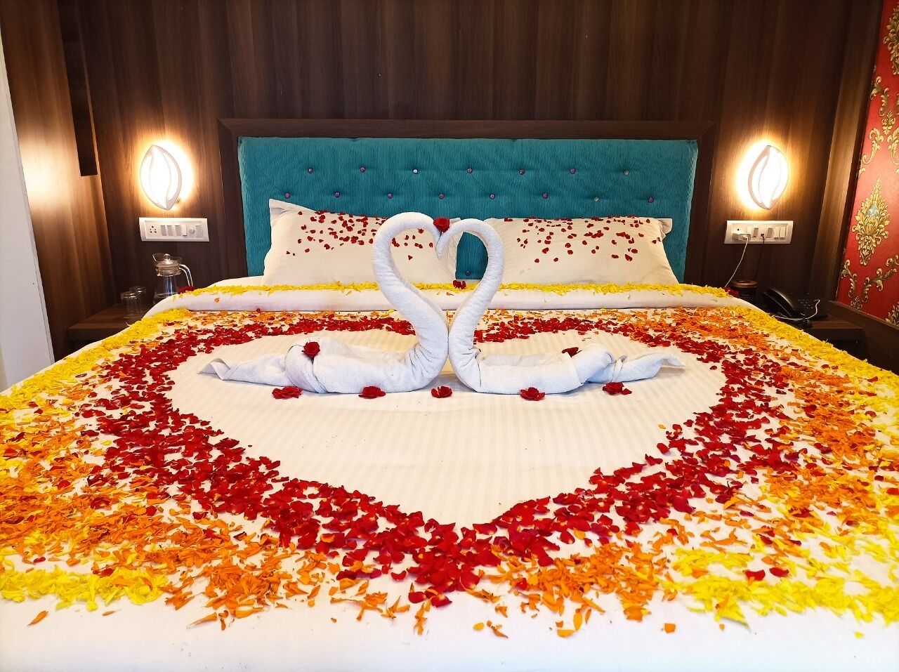 Uma cama decorada com pétalas de rosa em formato de coração e dois cisnes feitos de toalhas.