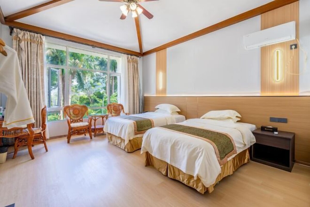 A hotel room with two beds, a desk, chairs, and a large window.