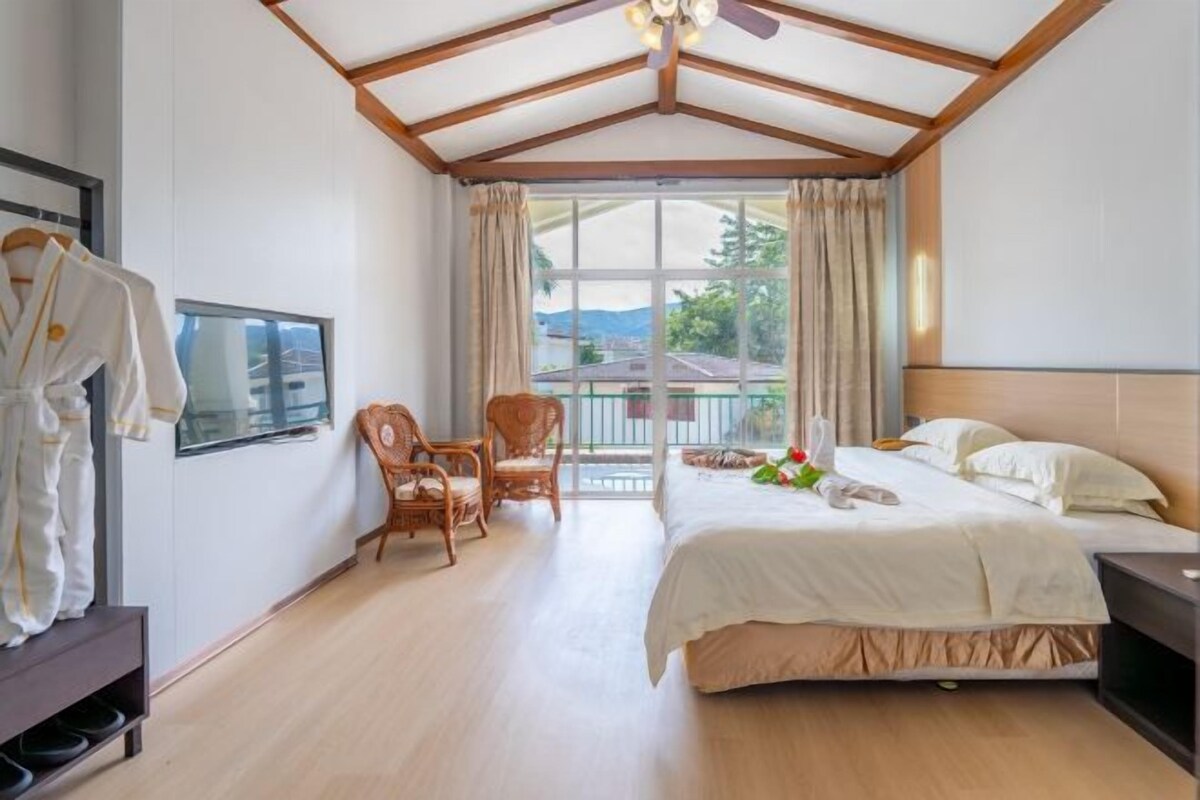 A bedroom with a large bed, a chair, a TV, and a window with curtains.
