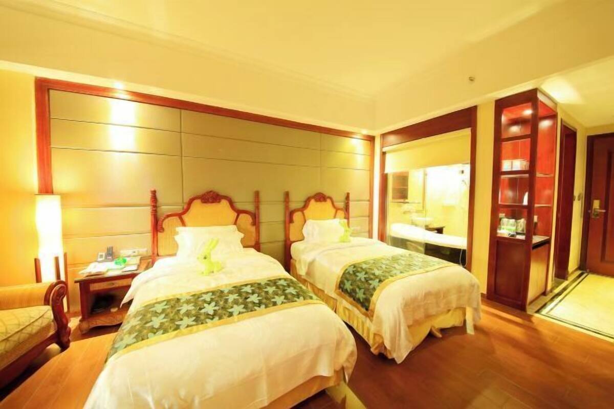 A hotel room with two beds, a bedside table, a lamp, a mirror, and a wardrobe.