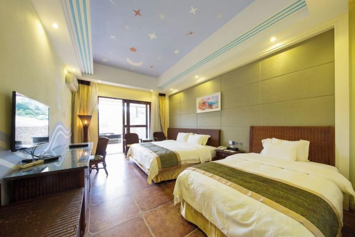 A hotel room with two beds, a desk, a TV, and a view of the outdoors.