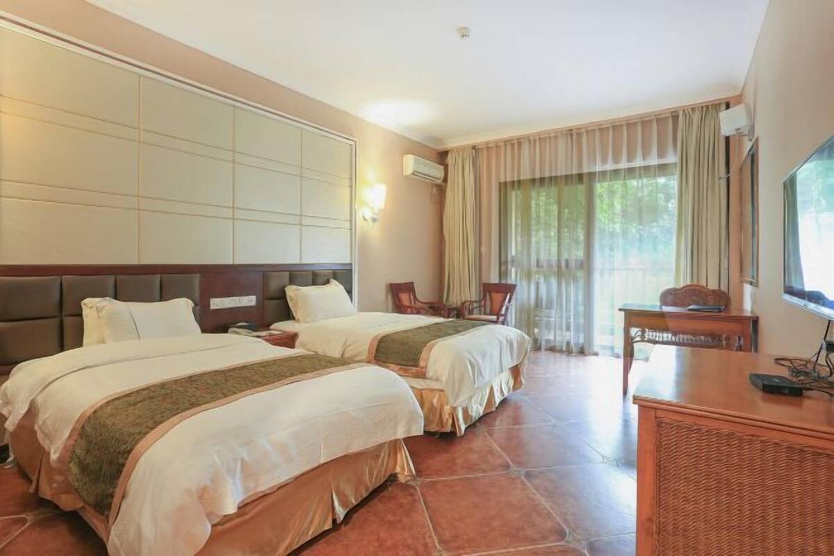 A hotel room with two beds, a desk, a chair, and a TV.