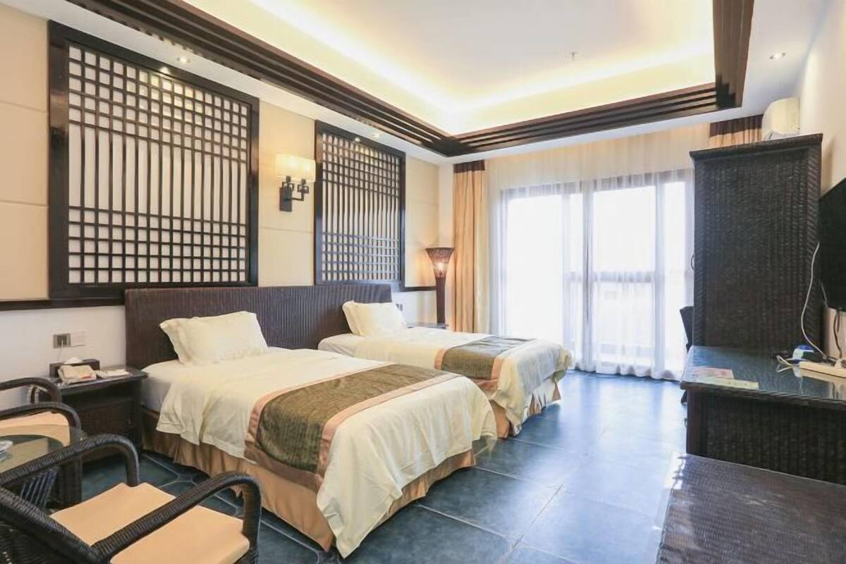 A hotel room with two beds, a desk, a chair, and a TV.