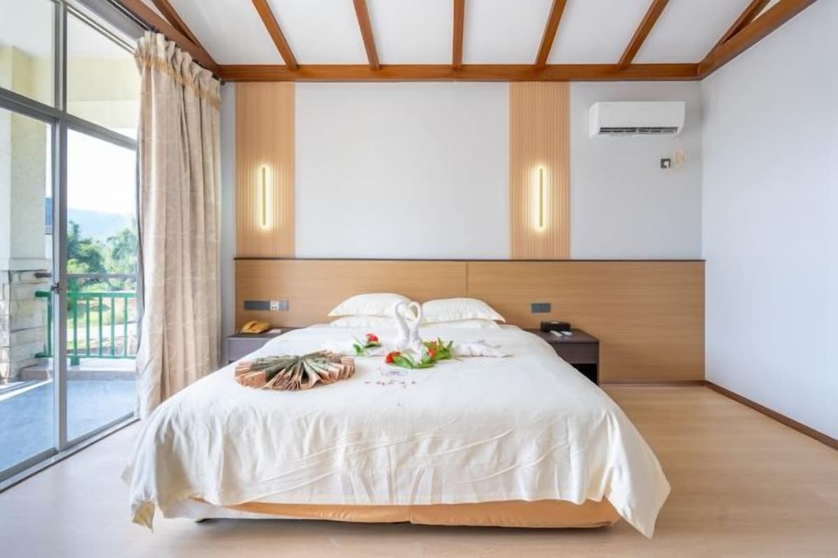 A hotel room with a large bed, a wooden headboard, a nightstand, and a view of the outdoors.