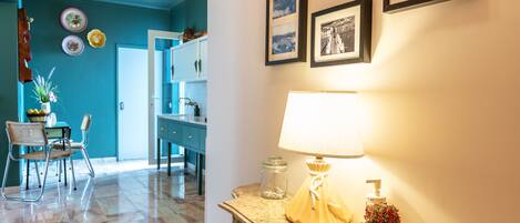 Un couloir avec un mur de couleur turquoise, un sol en marbre, une table avec une lampe et des tableaux encadrés accrochés au mur.