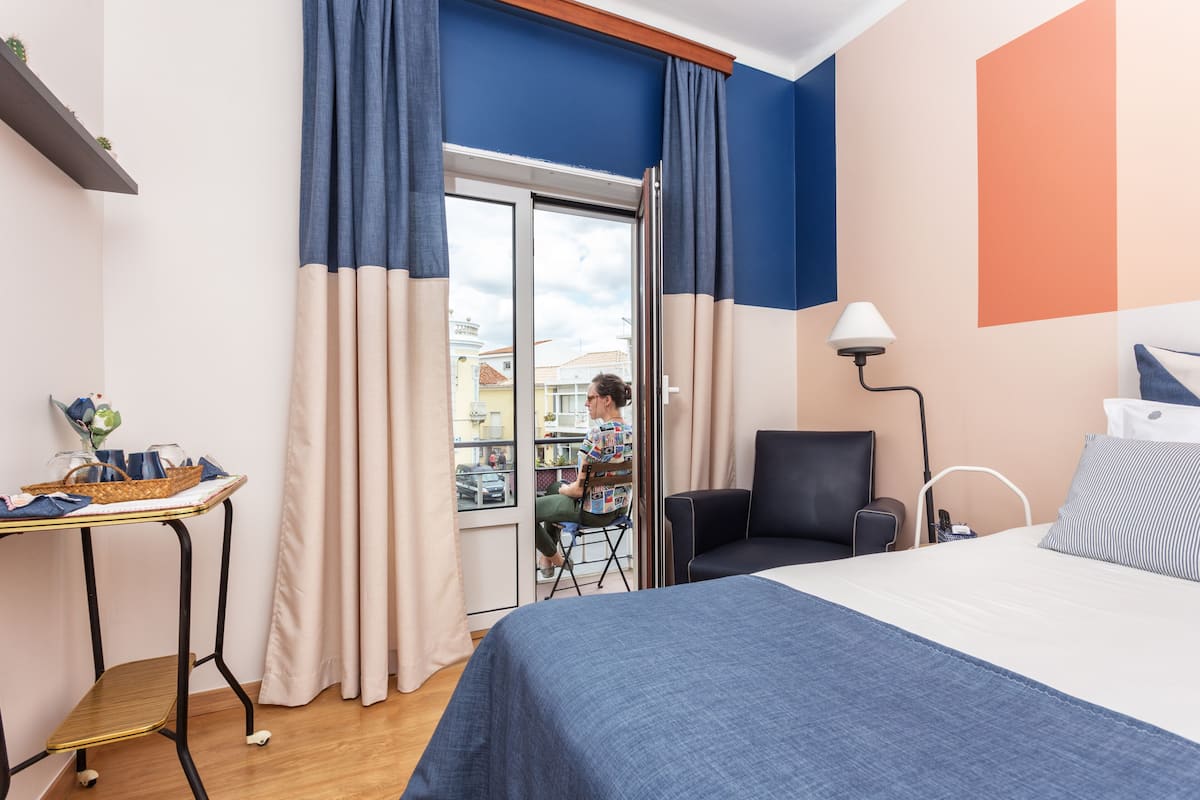 Hotellihuone, jossa on sänky, tuoli, kori sisältävä pöytä ja näkymä ulos.