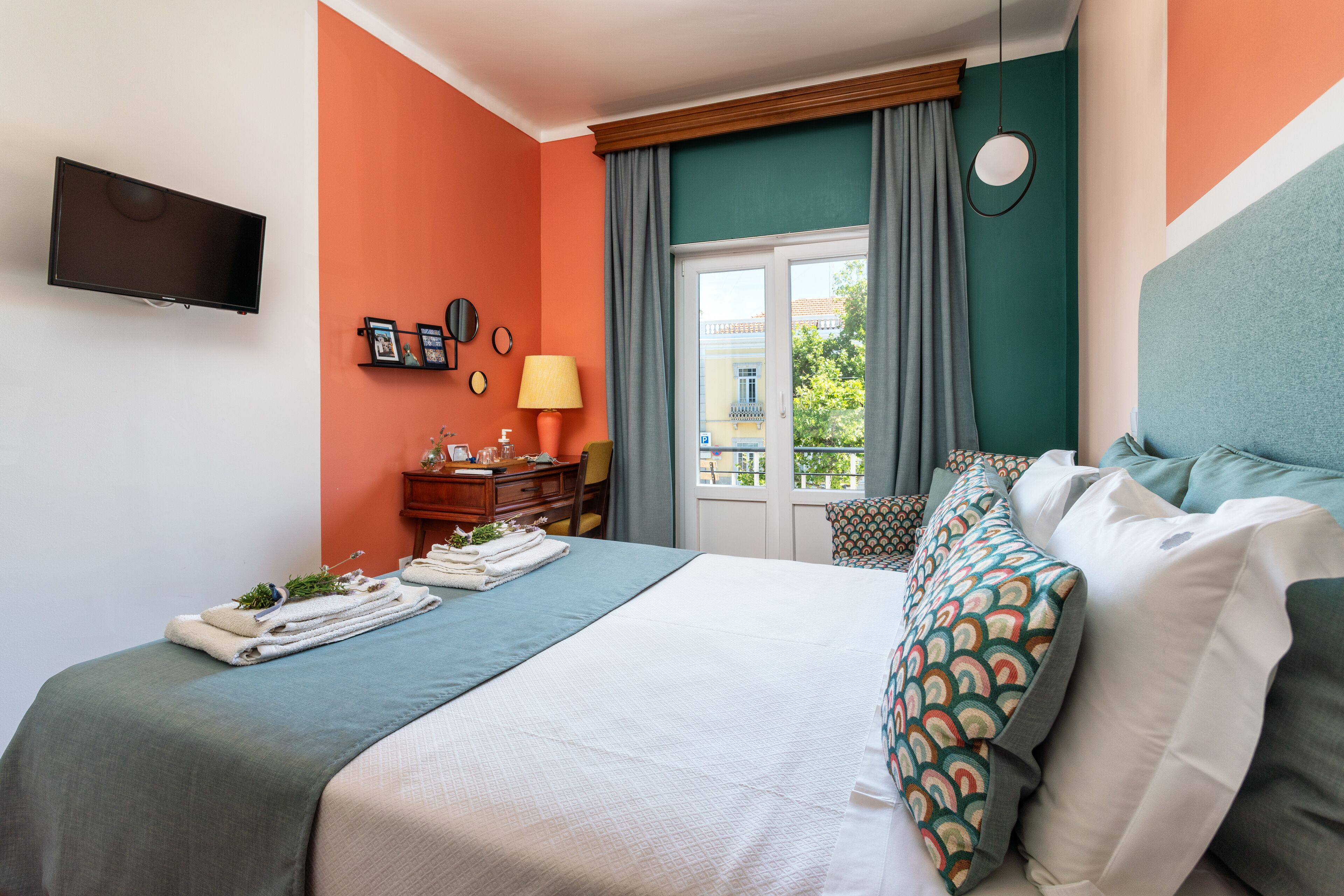 A hotel room with a bed, a TV mounted on the wall, a window with curtains, and a view of the outside.