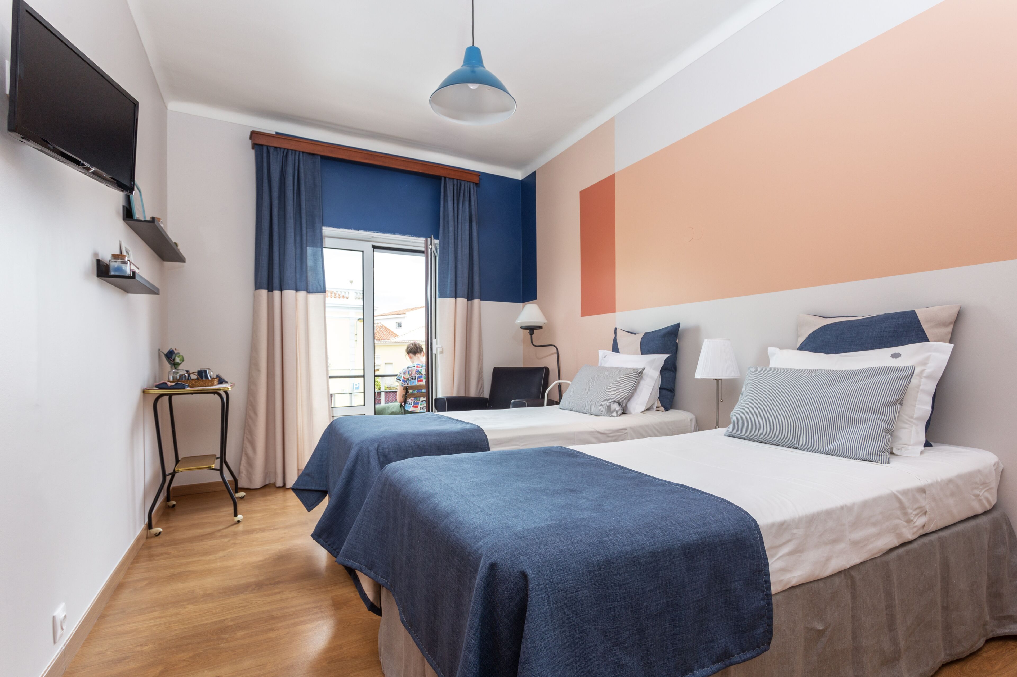 Habitación de hotel con dos camas, televisión, escritorio y ventana con cortinas.