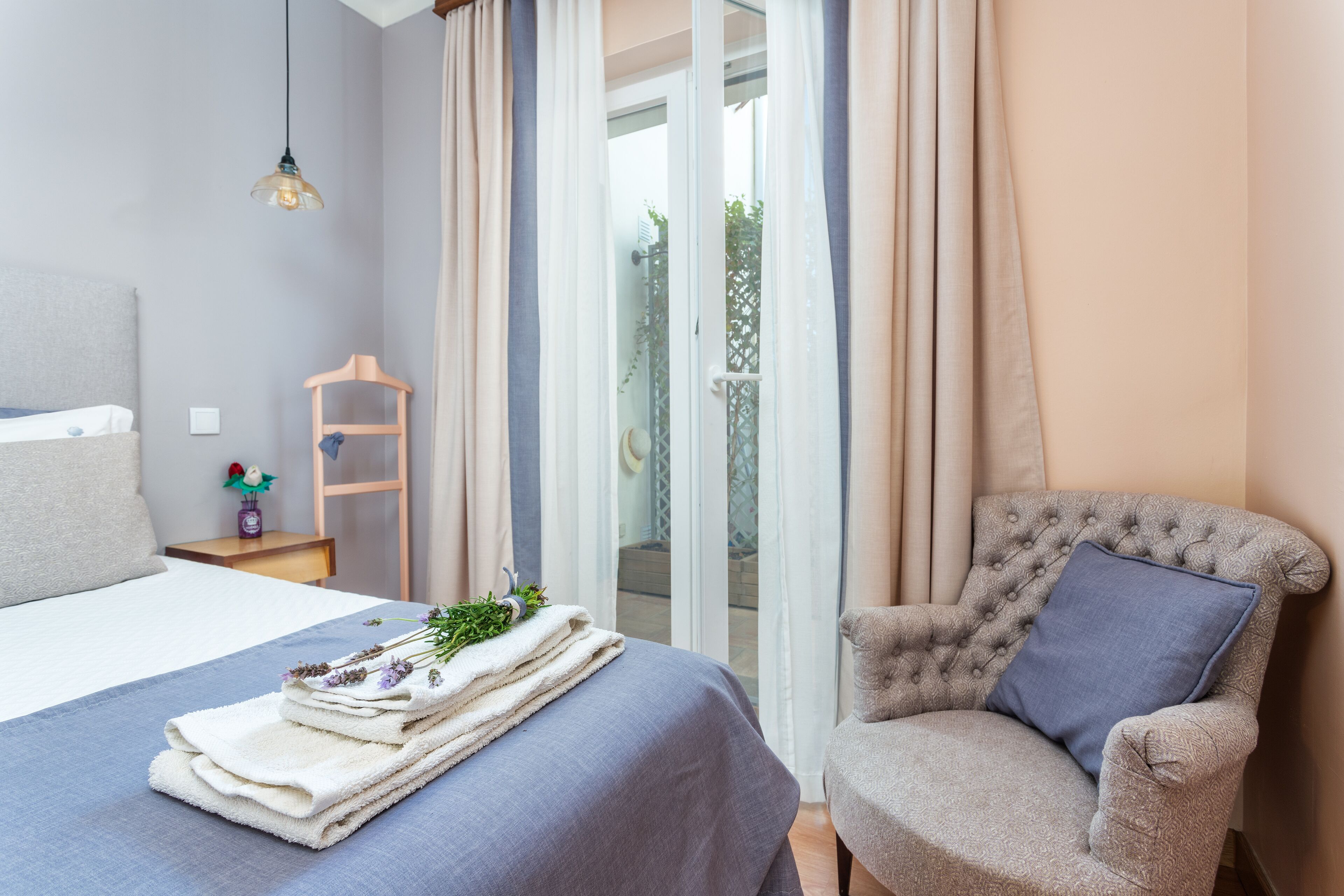 A bedroom with a bed, a chair, a small table, and a window with curtains.
