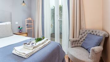 Un dormitorio con cama, una silla, una mesita y una ventana con cortinas.