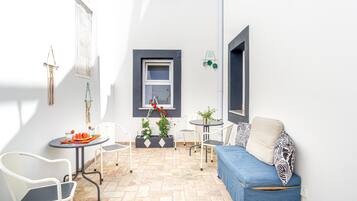 Une petite terrasse ensoleillée avec un canapé bleu, des chaises blanches, une petite table et des plantes en pot.