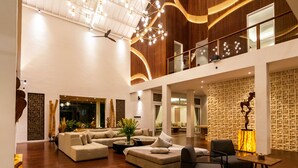 Ein geräumiger Wohnbereich mit hohen Decken, Holzvertäfelung und einer modernen Kronleuchter. Es gibt mehrere Sitzgelegenheiten, darunter ein großes Sofa und ein kleines Couches.