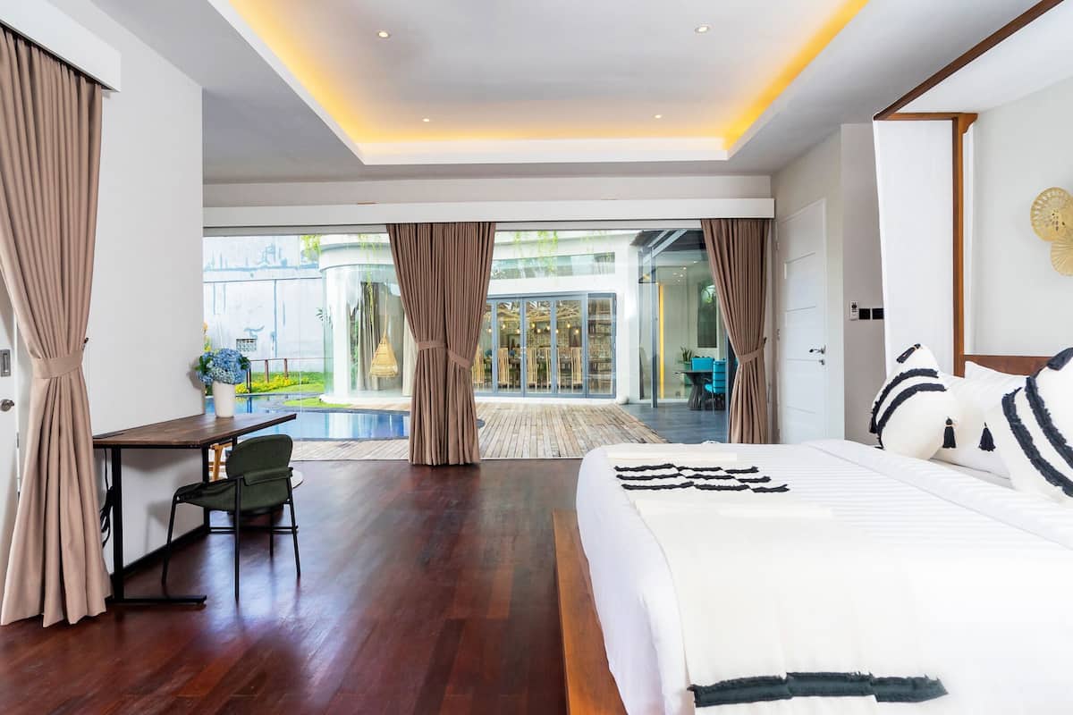 A modern hotel room with a large bed, a desk, and a view of a pool and garden.