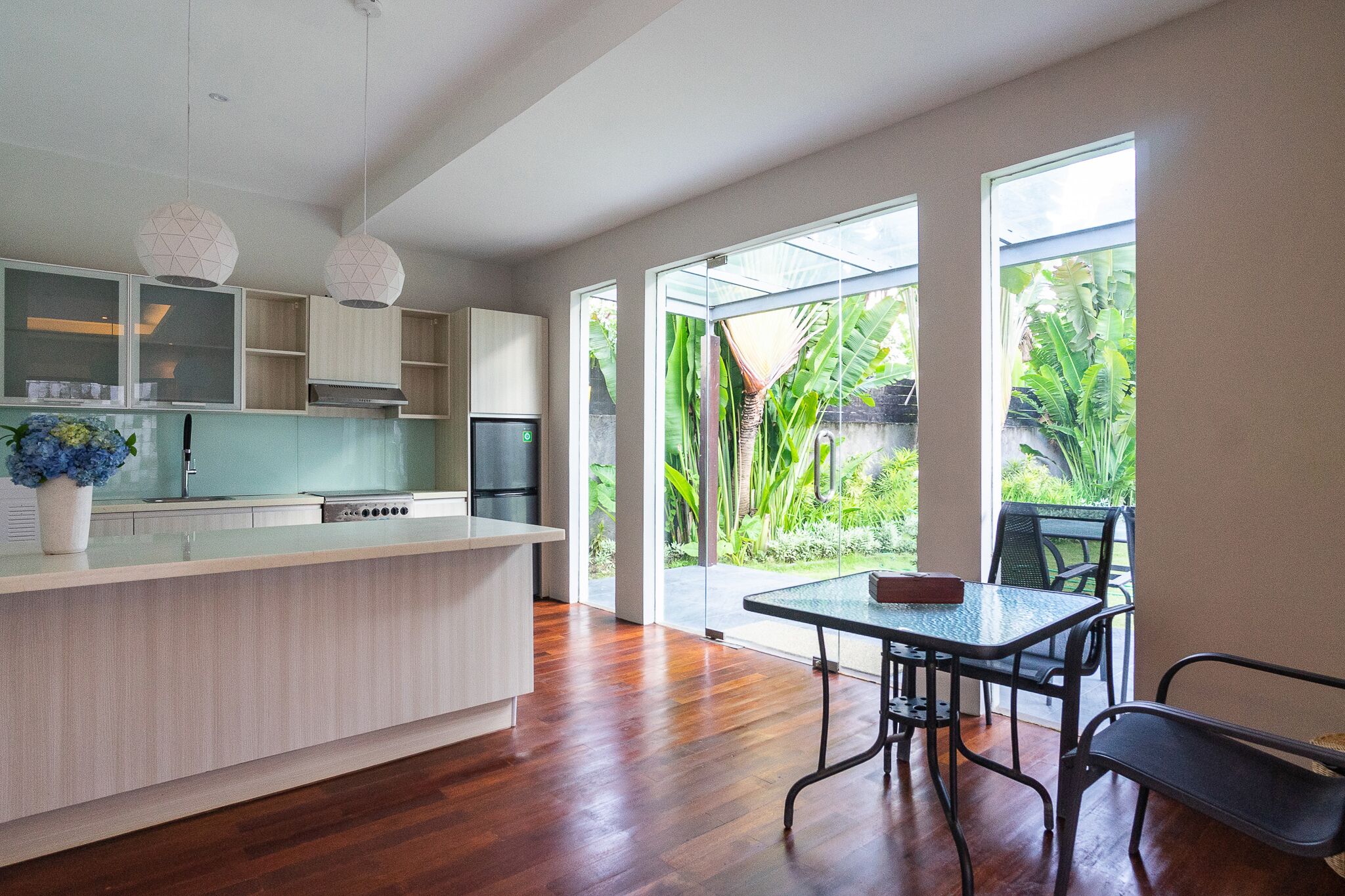 A modern kitchen with a large island, wooden flooring, and a dining area with a table and chairs.