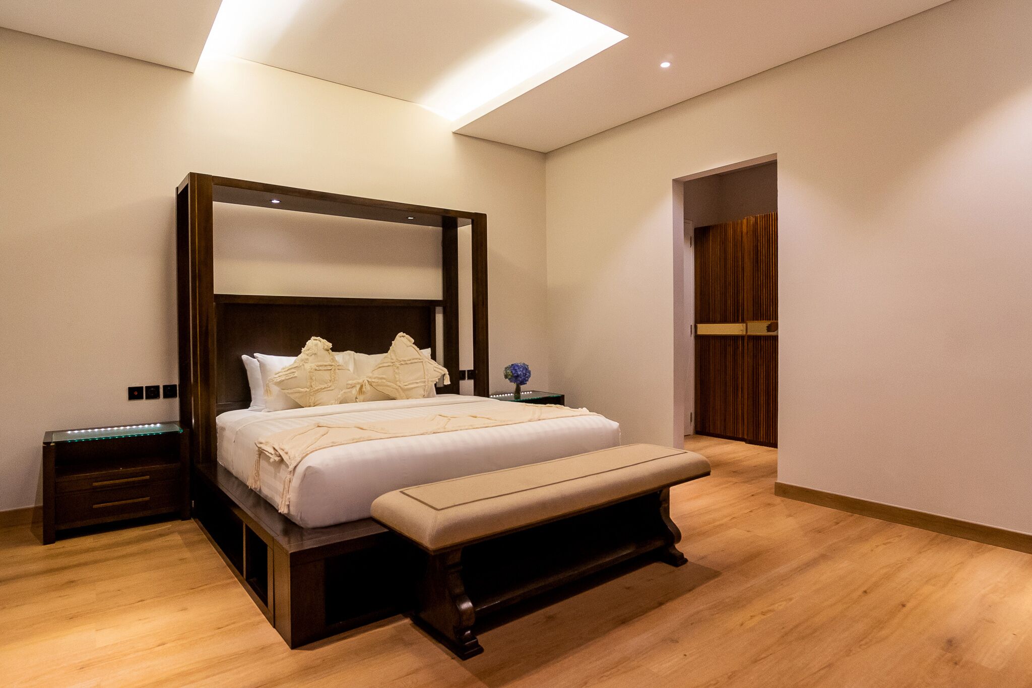 A modern bedroom with a large bed, wooden headboard, bedside tables, and a bench.