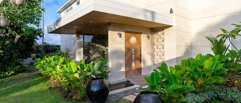 A modern building with a flat roof, a large wooden door, and a covered entrance area.