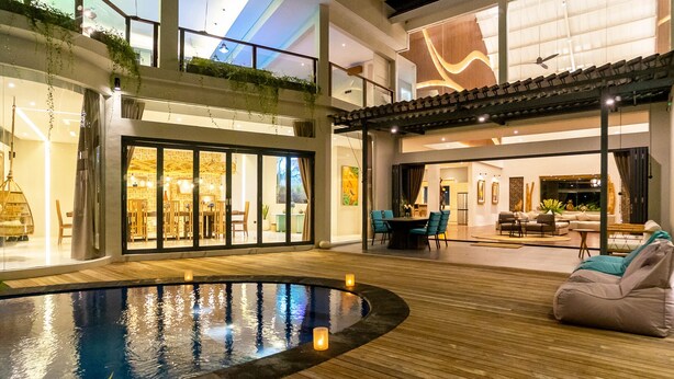 Ein moderner Poolbereich im Innenbereich mit Holzterrasse, Sitzgelegenheiten und einem durch Glas geschützten Essbereich.