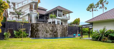Una casa moderna de varios pisos con piscina, un espacio exterior cubierto y abundante vegetación.