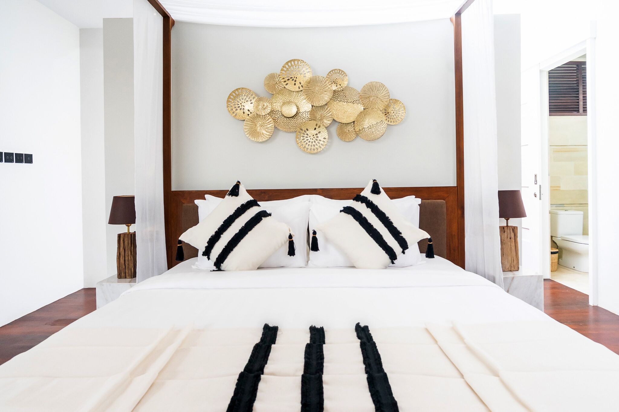 A modern hotel room with a large bed, a decorative wall piece, and a view of the bathroom.