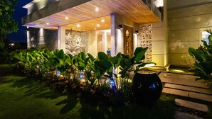 Ein modernes Haus mit überdachter Veranda, einem gut beleuchteten Garten und einer großen Zierwand.