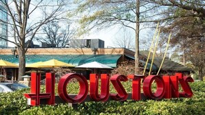 Ein großes, rotes Schild mit dem Schriftzug "HOUSTON'S", umgeben von Grünpflanzen und Bäumen.
