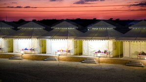 A row of tents with steps leading to the entrance, each tent illuminated from within. - Desert Over Night Camp & Resort (Jaisalmer)