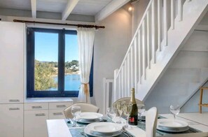A dining area with a table set for four, a bottle of champagne, and a view of a body of water through a window.