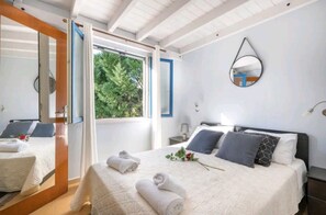 A bedroom with a bed, a nightstand, a mirror, and a window with a view of greenery.