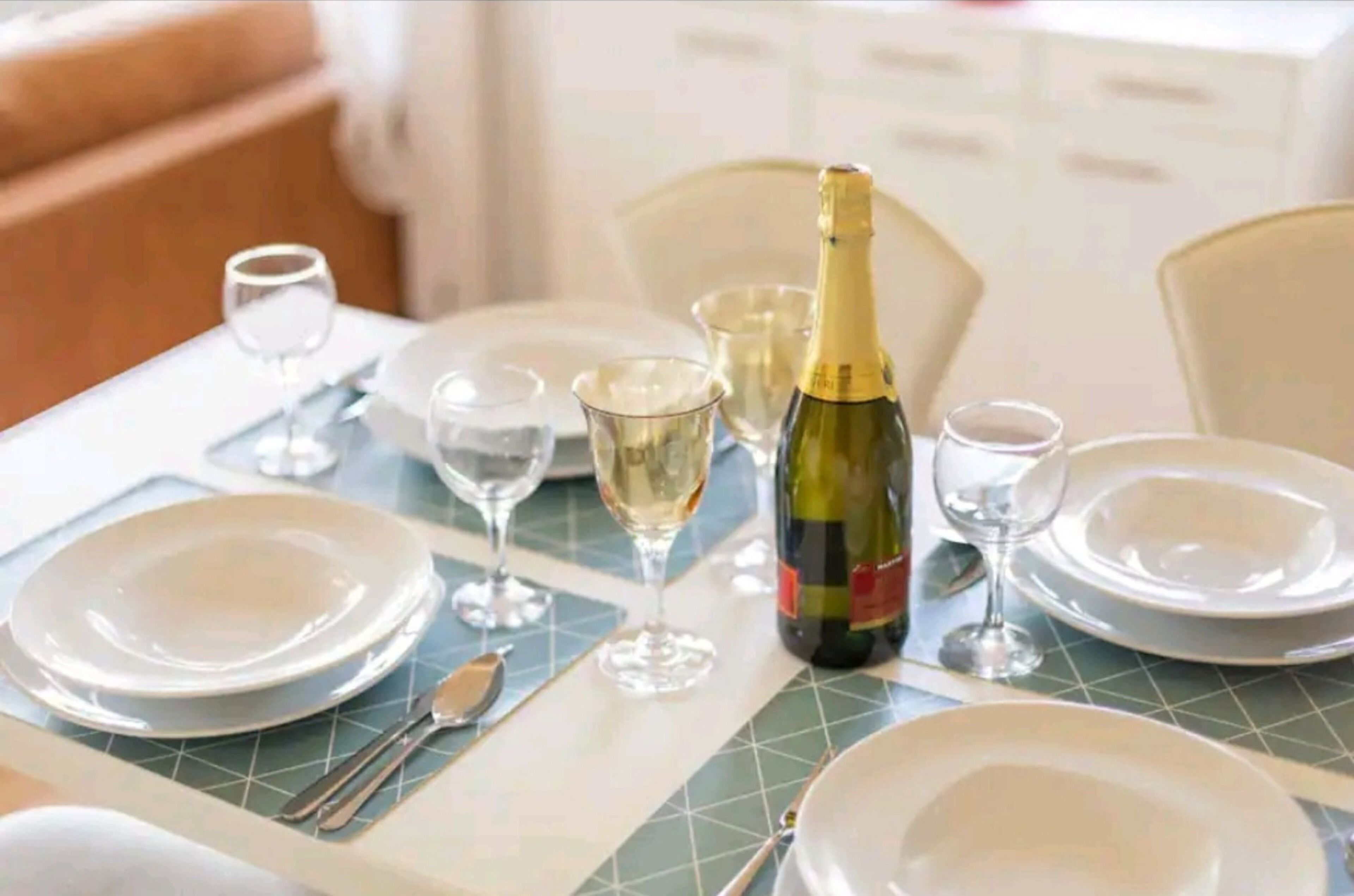 A dining table set with plates, wine glasses, and a bottle of wine.