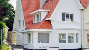 A two-story house with a red-tiled roof, white exterior walls, and a small front porch.