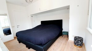 A modern bedroom with a large bed, a small stool, and a decorative vase.