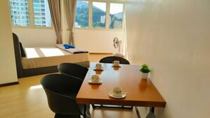 Une pièce avec une table en bois dressée pour quatre personnes, un canapé et une fenêtre donnant sur des bâtiments et des collines.