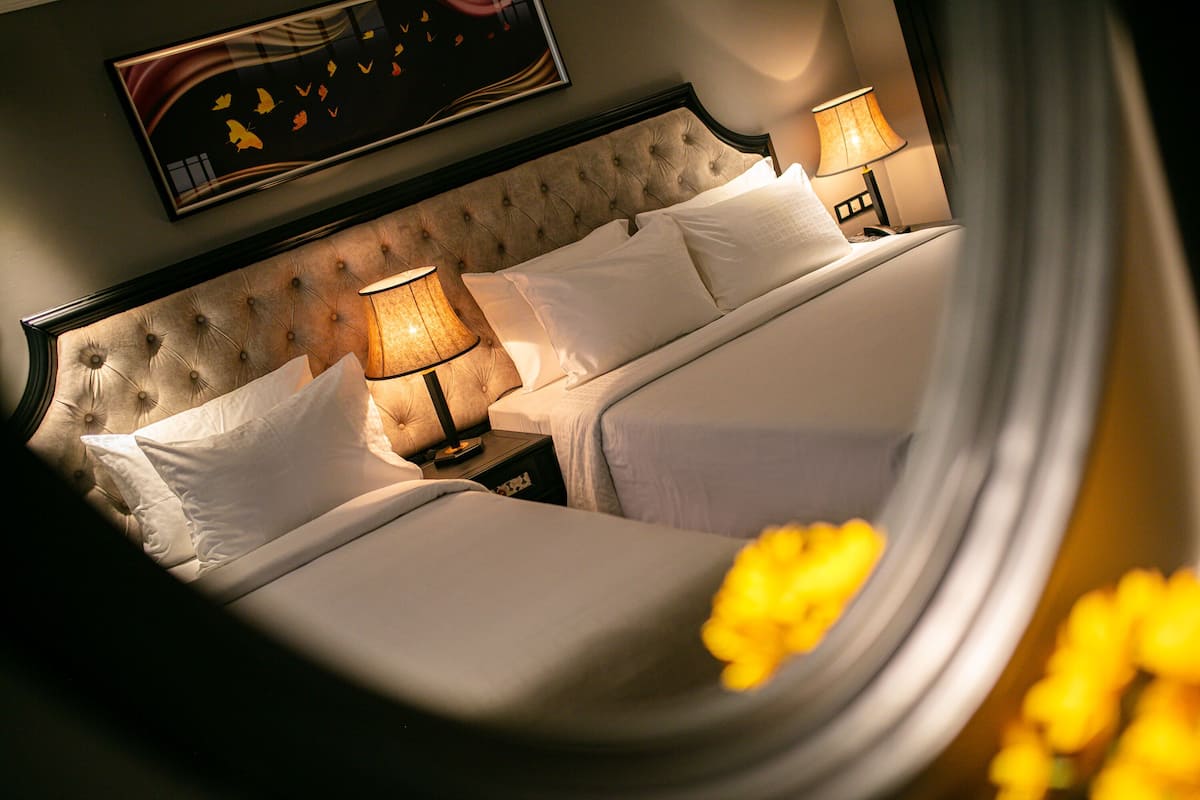 Une chambre d’hôtel avec une tête de lit capitonnée, deux lits avec du linge de lit blanc, des lampes de chevet et une œuvre d’art encadrée au mur.