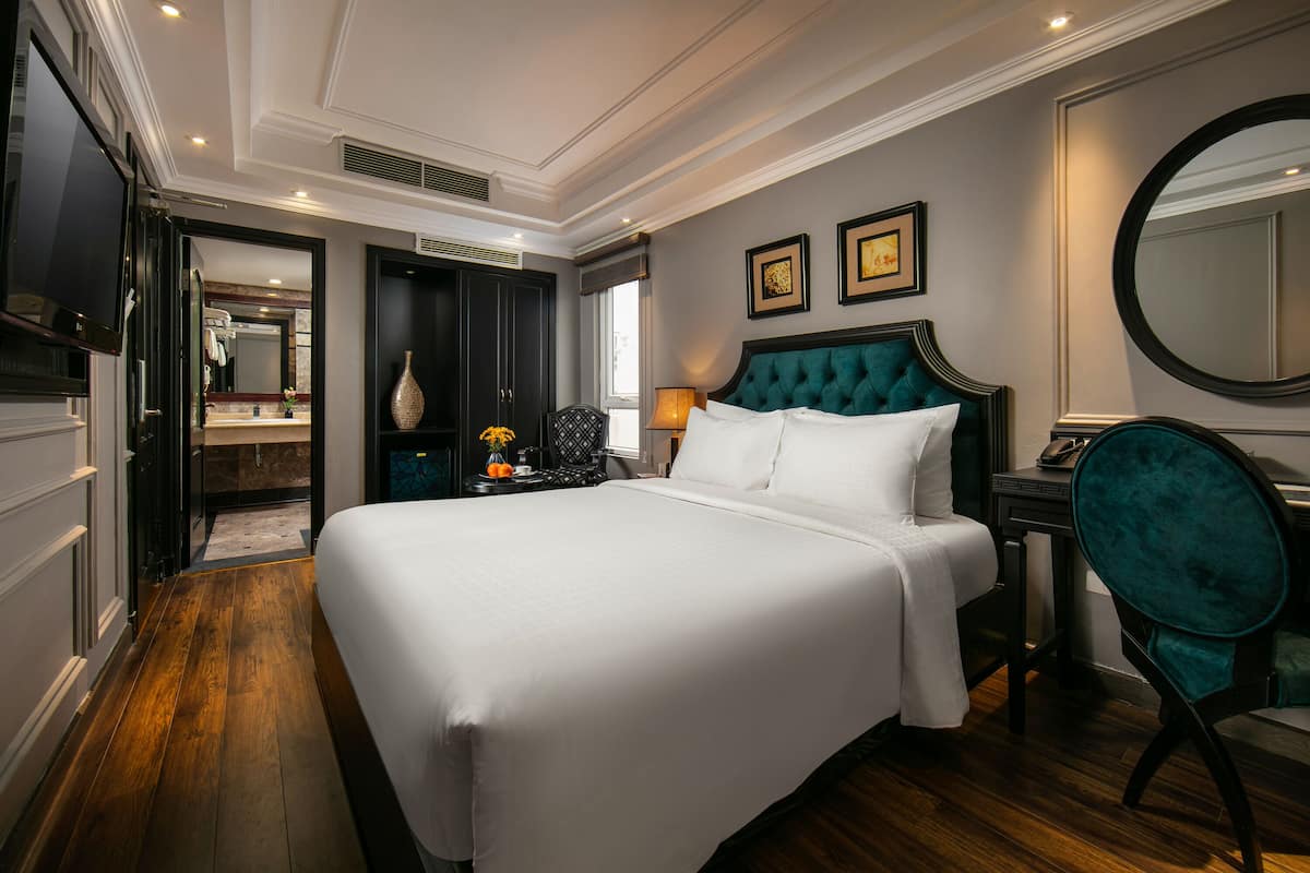 Une chambre d’hôtel avec un grand lit, une coiffeuse avec un miroir, une chaise et un bureau avec une lampe.