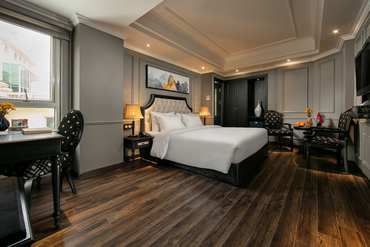 Une chambre d’hôtel avec un grand lit, un bureau avec une chaise, une télévision et une fenêtre donnant sur des immeubles.